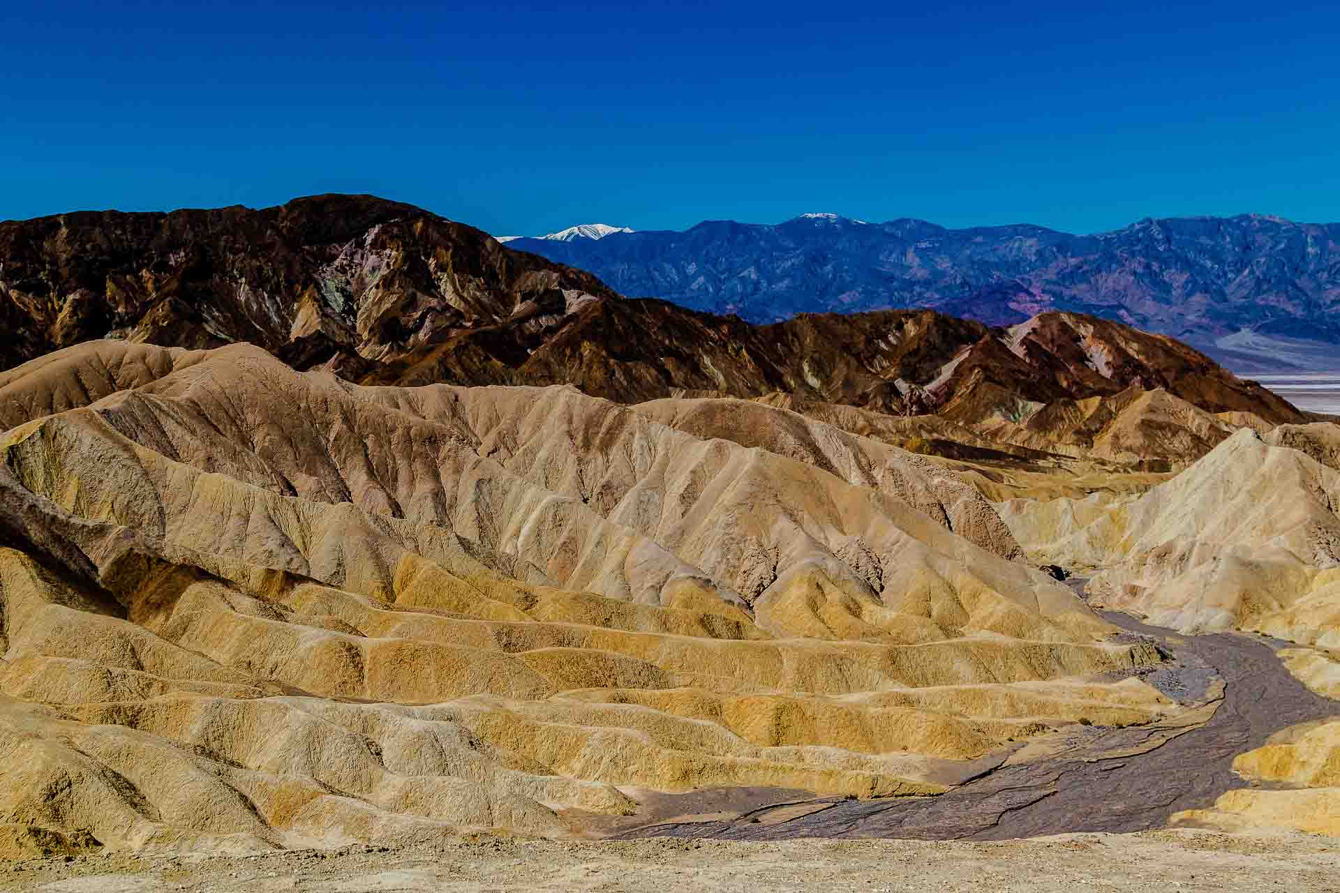 Mojave desert scrub and eroded ridges under a cloudless blue sky